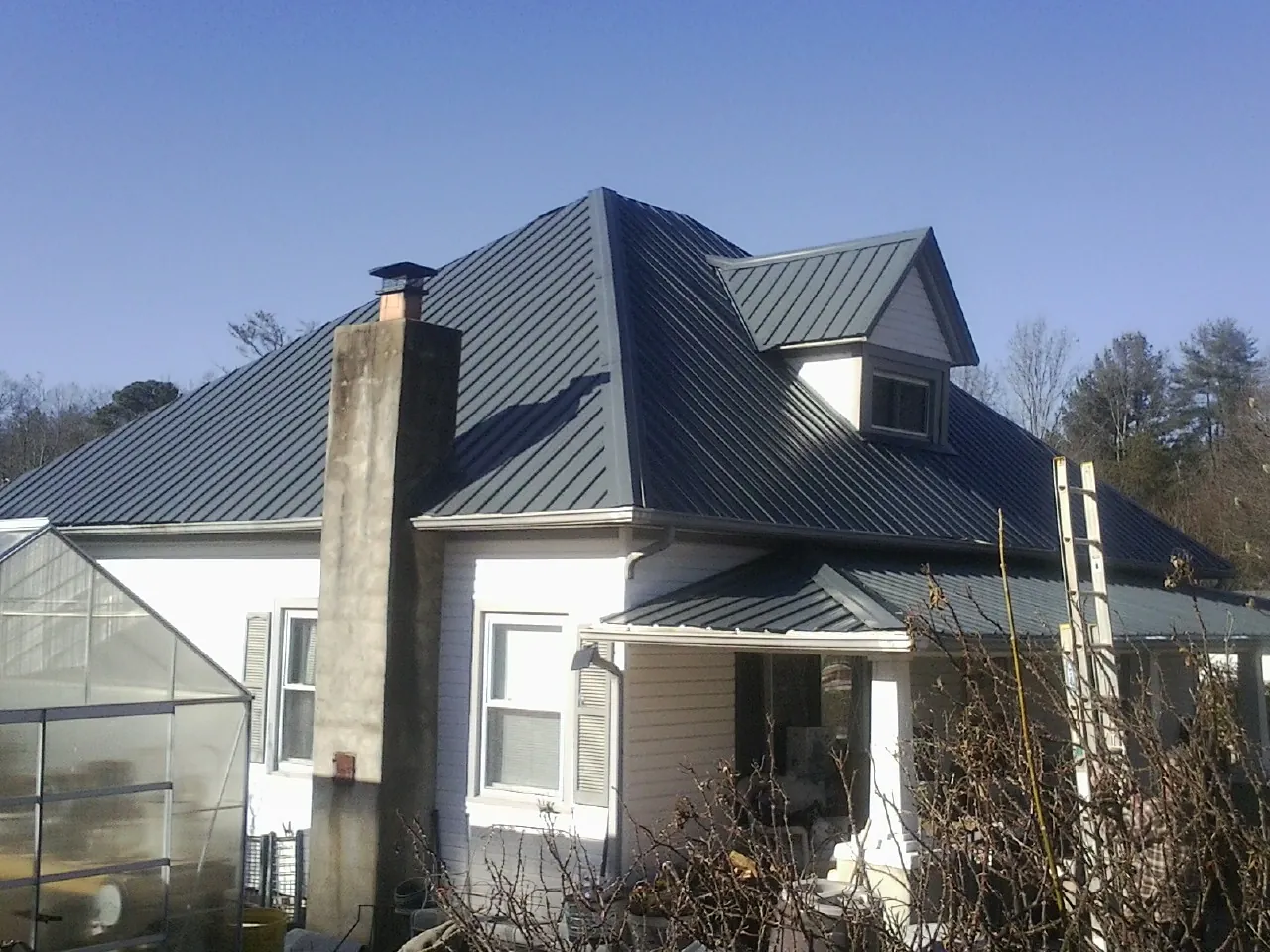 Dark blue standing seam metal roof on a white farmhouse with dormer — Slate & Tile Roof Repair by Roofing Brothers in North