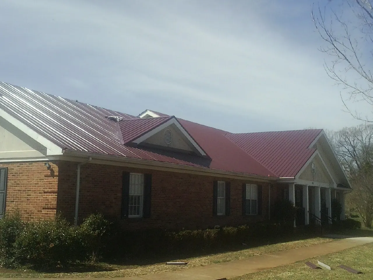 Red metal roof with gabled entries on a long brick building, from a Hail Damage Roof Repair job in North