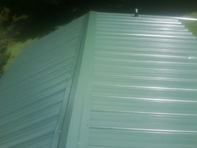 New green metal panels meeting at the ridge of a roof — Flat Roof Repair work by our crew in North