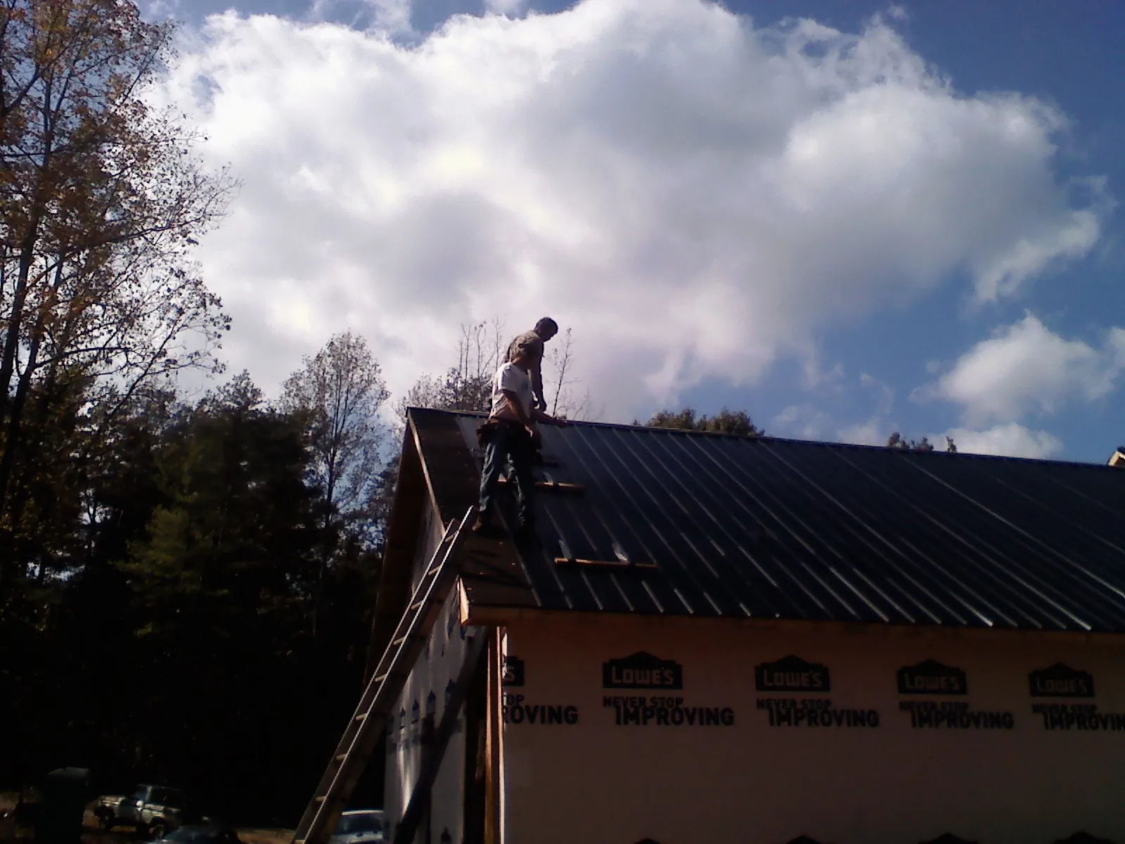 Roofer fastening dark metal panels high against a cloudy sky, from a Roof Inspection job in North