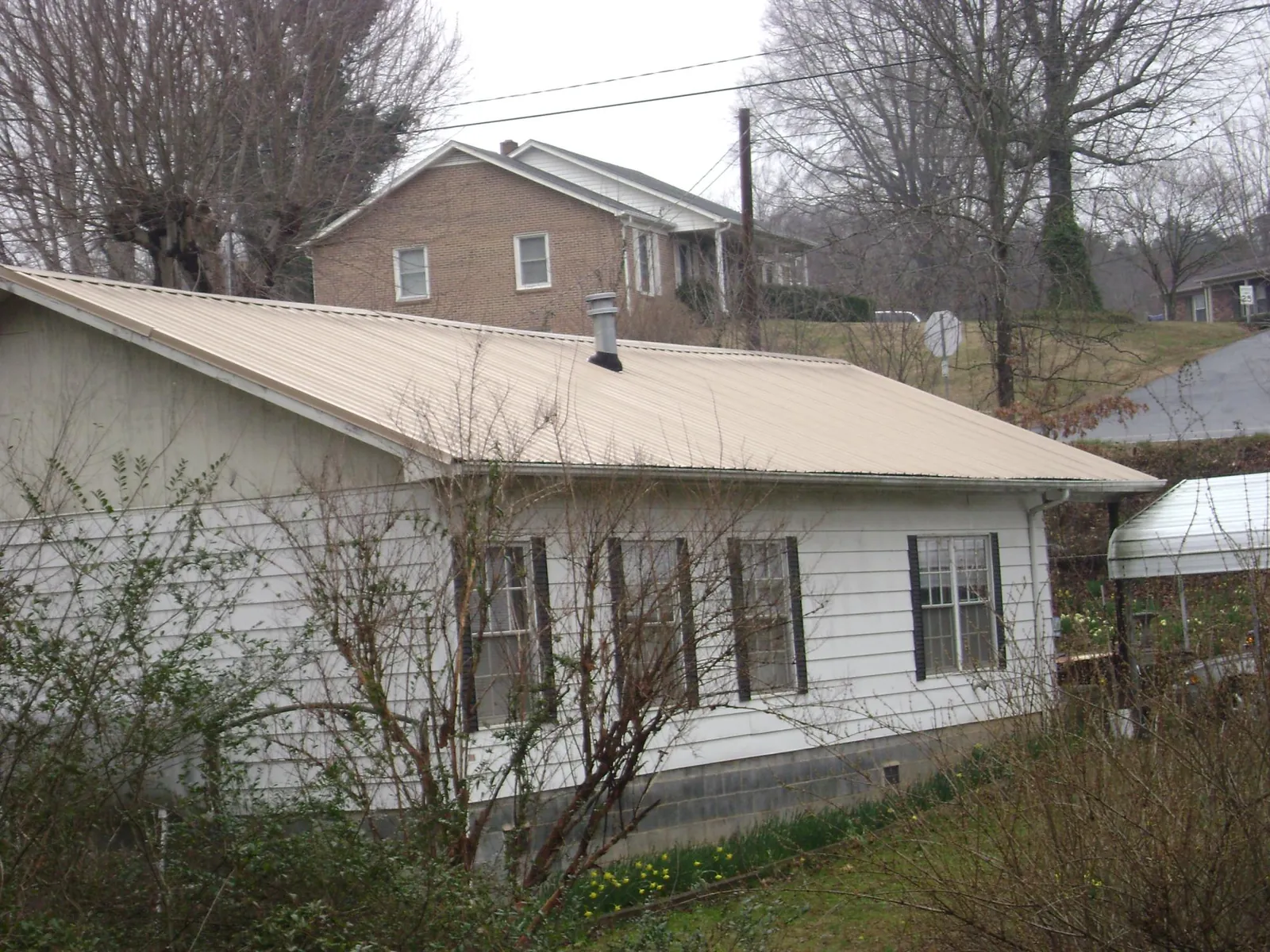 Tan metal roof on a white sided house set into a hillside — Commercial Roofing by Roofing Brothers in North