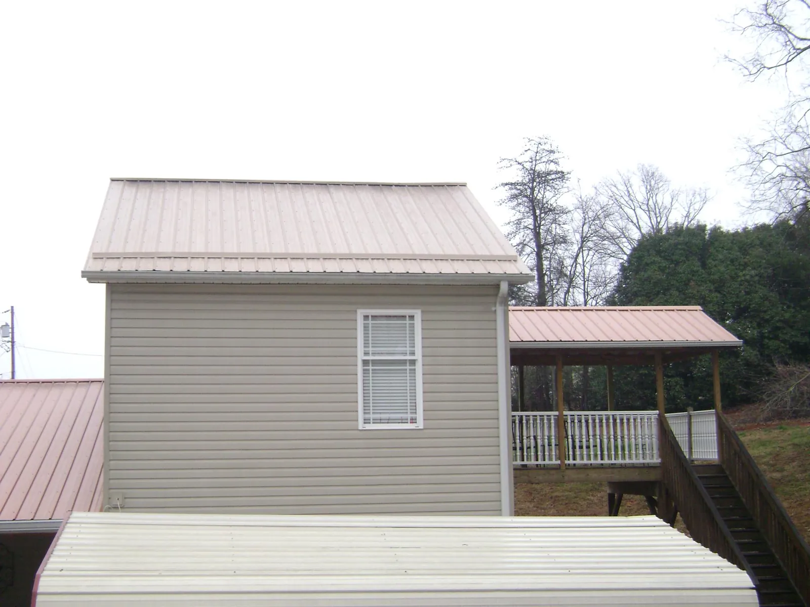 Tan metal roofs on a two story addition and attached porch, from a Roof Replacement job in North